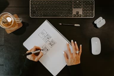 Hands sketching a wireframe in a notebook on a dark desk